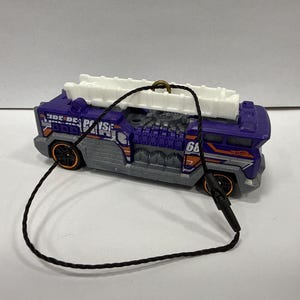 May include: A die-cast toy fire truck in purple and silver with a white ladder on top. The toy has black wheels with orange rims and the number 68 on the side. A black string is attached to the top.