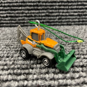 May include: A small, orange and green toy backhoe with a green string attached. The backhoe has a black and white sticker on the side that says "1170".