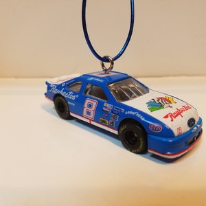 May include: A blue and white Ford race car ornament with the number 8 and the word "Runklestos" on the side. The car has a red, white, and blue checkered flag design on the hood.