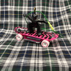 May include: A black figure on a pink and black skateboard with a zebra print design. The figure is holding a green string and is in a skateboarding pose. The skateboard has white wheels.