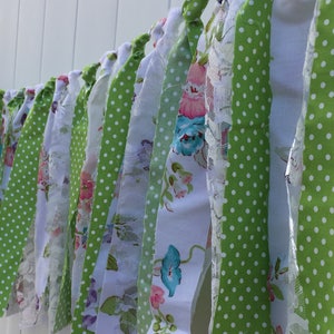 May include: A green and white fabric banner with floral and polka dot patterns. The banner is made of strips of fabric that are tied together.