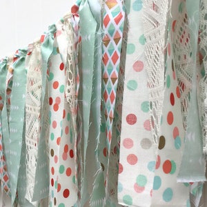 May include: A handmade fabric garland with a mix of patterns, including polka dots, geometric shapes, and lace. The garland is in shades of mint green, coral, and white.
