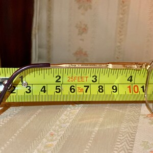 May include: Gold-tone eyeglasses with a purple arm, measured with a yellow tape measure. The glasses are marked "Disney 14 BROWN MARBLE 120". The tape measure shows a length of approximately 4 inches.