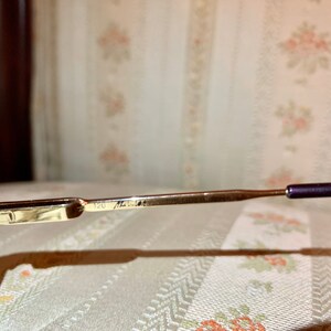 May include: Close-up of a pair of eyeglasses. The frames are gold-colored with a rectangular design on the front. The temple arms are a gradient from gold to brown, ending with a dark purple earpiece. The number "120" and other text are visible on the frame.