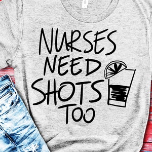 Puede incluir: Una camiseta gris con el texto "Nurses Need Shots Too" en letras negras. Una ilustración en blanco y negro de un vaso de chupito con una rodaja de lima está al lado del texto.