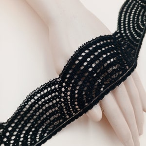 May include: Black lace trim with a delicate, circular pattern. The trim is approximately 1 inch wide and has a soft, flexible texture.