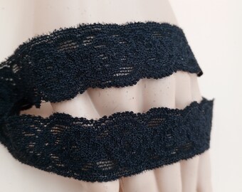 May include: Black lace trim with a scalloped edge. The trim is shown folded in half.