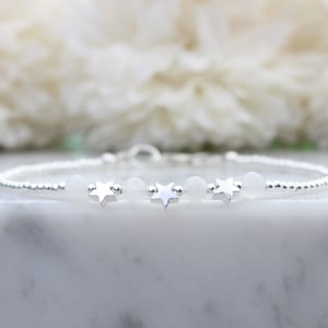Op de afbeelding: Een zilveren armband met drie sterbedels en witte kralen.