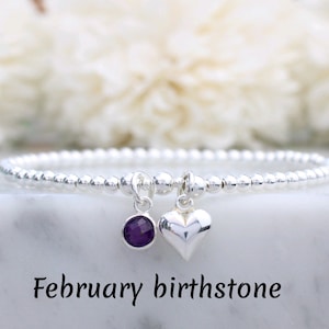 Puede incluir: Un brazalete de cuentas de plata con una pequeña piedra preciosa de amatista y un dije de corazón de plata. Piedra de nacimiento de febrero.