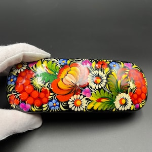 May include: A black rectangular box with a floral design painted on the top. The design features red, yellow, orange, green, blue, and white flowers and berries.