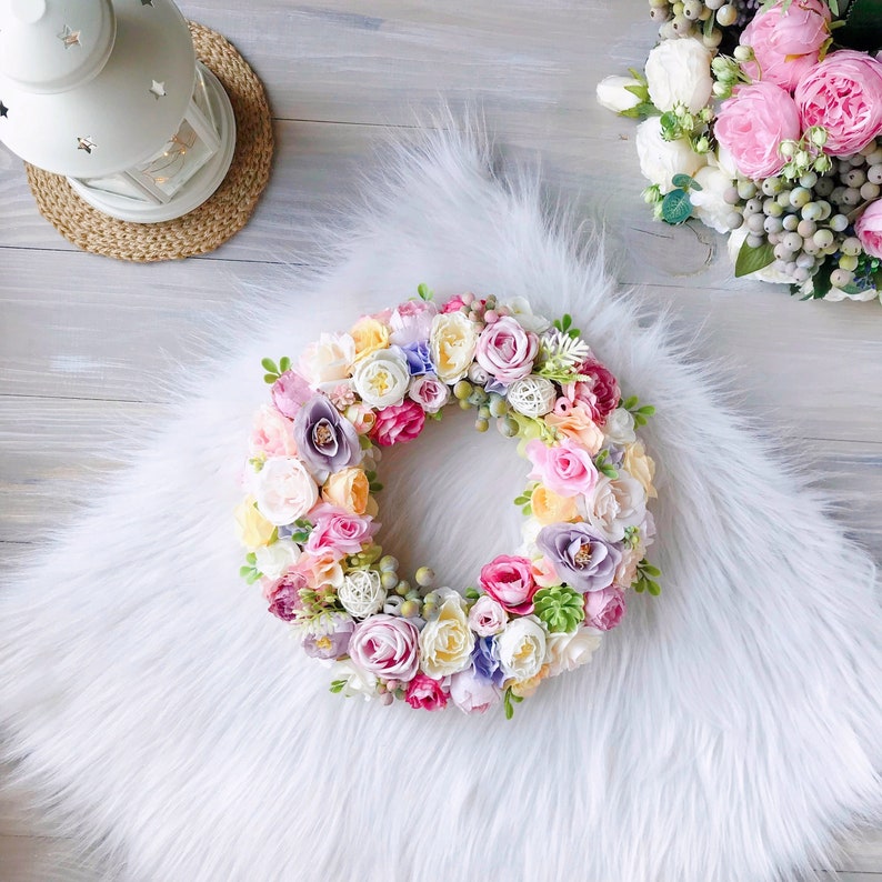 May include: A pastel-colored floral wreath with pink, white, yellow, and purple flowers. The wreath is made of silk flowers and is perfect for decorating a home or office.