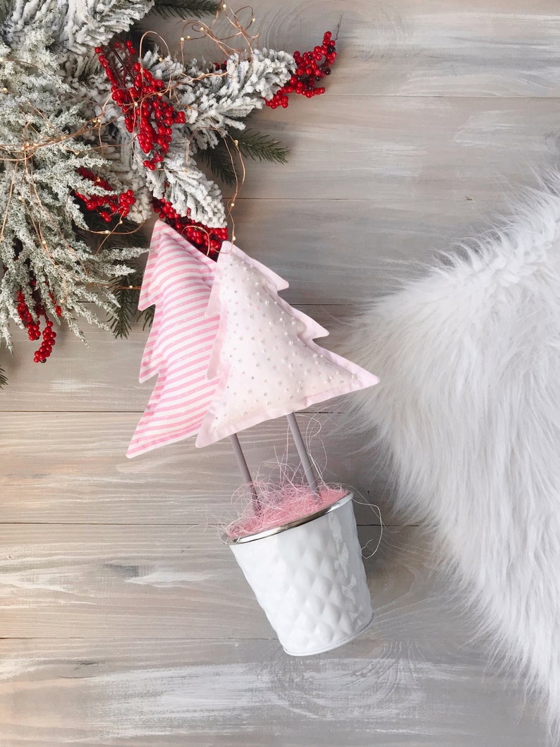May include: Two pink fabric Christmas trees in a white metal pot with pink and white filler. The trees are decorated with white polka dots and pink stripes.