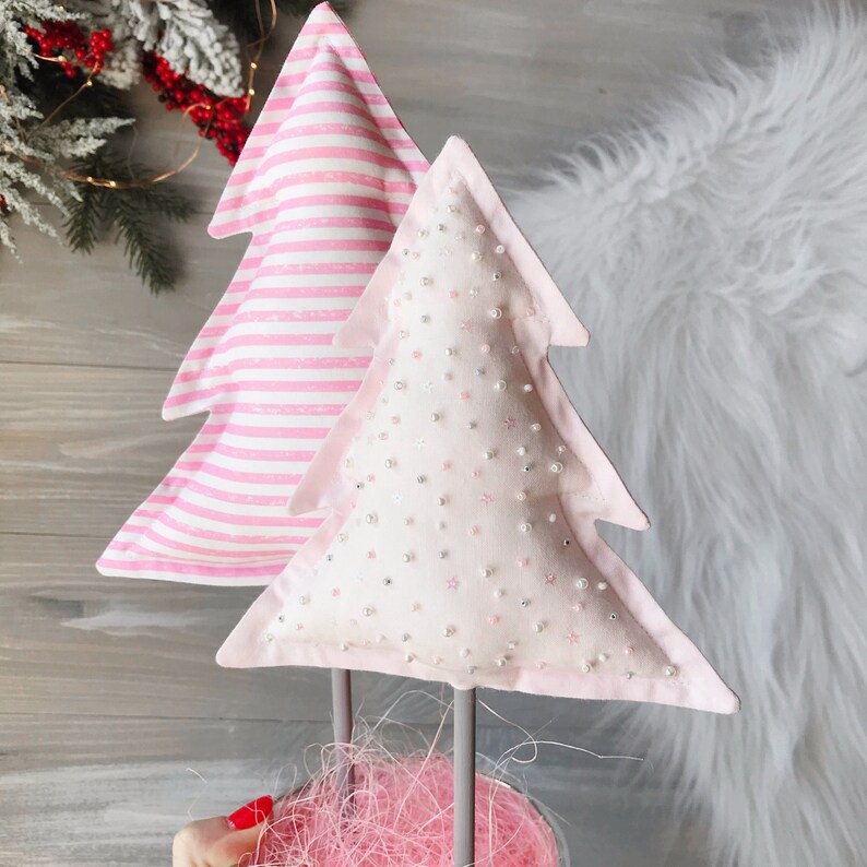 May include: Two pink and white Christmas tree decorations. One tree is striped and the other is covered in white beads.