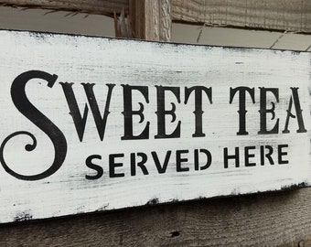 Può includere: Un cartello in legno bianco con lettere nere che recita "Sweet Tea Served Here". Il cartello ha un aspetto usurato e vintage.