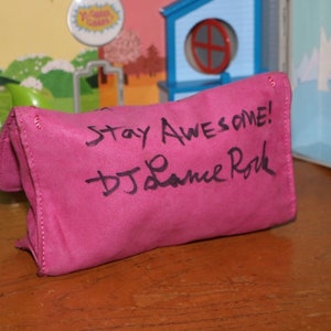 May include: A pink fabric pouch with the words "Stay Awesome!" and a signature that reads "DJ Lance Rock" written in black marker.