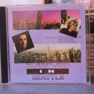 May include: A purple CD case with a cityscape background and the text "Sleepless in Seattle" featuring the songs "When I Fall in Love", "With One Look", and "Will You Be There".