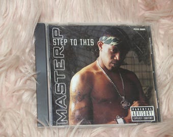 May include: A CD case with a black background and the words "MASTER P STEP TO THIS" in white. The cover features a man wearing a camouflage bandana and a gold chain.