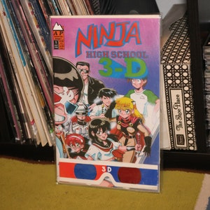 May include: A comic book cover with the title "Ninja High School 3-D". The cover features a group of characters in a school setting, including a ninja, a girl with a sword, and a boy with a gun. The comic book is in a plastic sleeve.