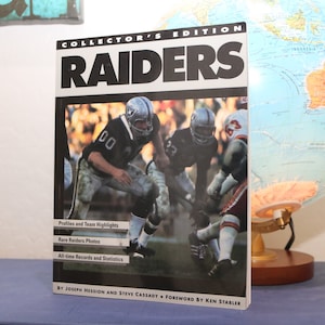 May include: A collector's edition book about the Raiders football team. The cover features a black and white photo of players in action. The title "RAIDERS" is in large, bold, black letters. The book includes profiles, team highlights, rare photos, and all-time records and statistics. By Joseph Hession and Steve Cassady. Foreword by Ken Stabler.