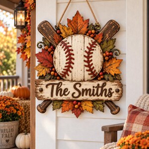 May include: A decorative wall hanging featuring a central baseball design with red stitching, crossed wooden baseball bats, and autumn-colored maple leaves and berries. A rectangular wooden sign below displays the text The Smiths.