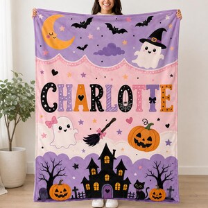 May include: A soft fleece blanket featuring a Halloween theme with a purple and pink gradient background. The design includes a yellow crescent moon, bats, a ghost in a witch hat, a jack-o'-lantern, a broom, and a haunted house. The name CHARLOTTE is printed in large, colorful, patterned letters across the center.