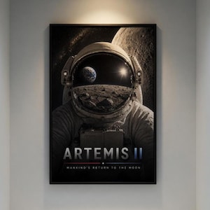 May include: A framed print featuring an astronaut in a spacesuit, with the Earth and the moon visible through the helmet visor. The print has the text "ARTEMIS II" and "MANKIND'S RETURN TO THE MOON" in white text on a black background.