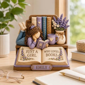 May include: A decorative figurine featuring a brown-haired figure lying on a shelf reading a book, with a lavender mug, a vase of purple flowers, and a large open book displaying the text 'JUST A GIRL WHO LOVES BOOKS' and the name 'EMILY'.