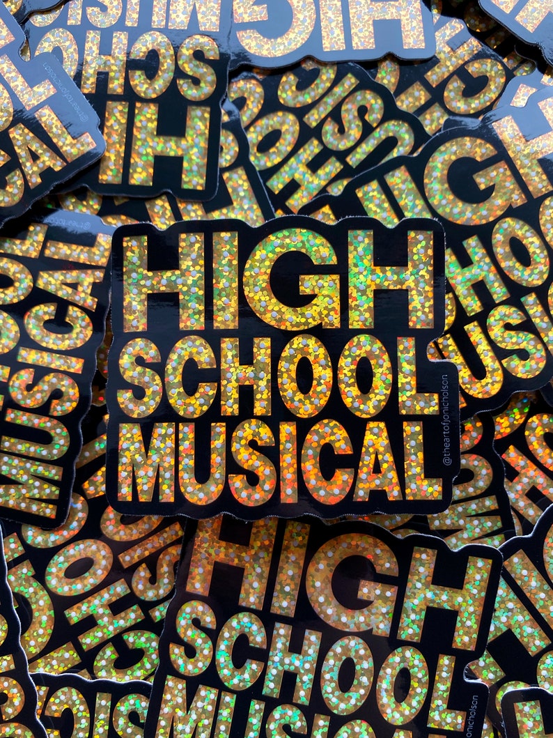 May include: A close-up of a stack of gold glitter stickers that say "High School Musical" with a black background. The stickers have a holographic finish and are perfect for adding a touch of sparkle to any project.