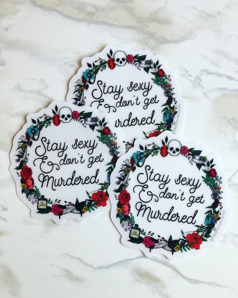 May include: Three round stickers with a floral wreath design. The wreath is made up of flowers, leaves, and other objects like a skull, a gun, and a bottle. The text on the stickers reads "Stay sexy & don't get murdered".