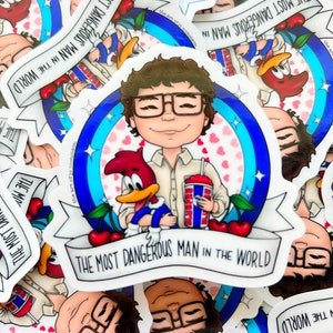 May include: A white sticker with a cartoon illustration of a man with brown hair and glasses holding a red cartoon bird and a blue and red slushie cup. The man is wearing a blue shirt and the background is blue with white hearts. The sticker has the text "The Most Dangerous Man in the World" on a white banner.