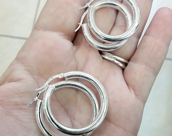 May include: A pair of silver hoop earrings with a double hoop design. The earrings are shown on a hand.