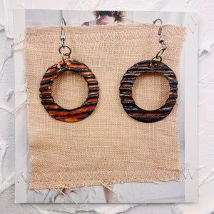 Peut inclure: Une paire de boucles d'oreilles créoles rayées orange et noires avec des crochets argentés.