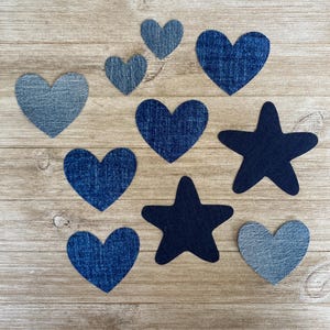 May include: A collection of fabric patches in various shades of blue denim, featuring six heart-shaped cutouts and two star-shaped cutouts. The patches display different textures and washes of denim fabric, ranging from light blue to dark navy blue.