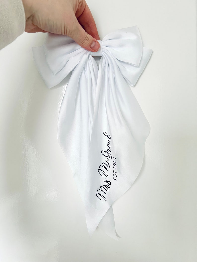 May include: White satin bow with a long tail, featuring the text "Mrs. McGreat EST 2024" in black script.