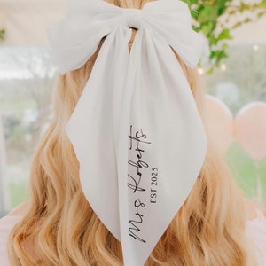 May include: White satin hair scarf with a large bow and the text "Mrs. Roberts EST 2025" printed in black.