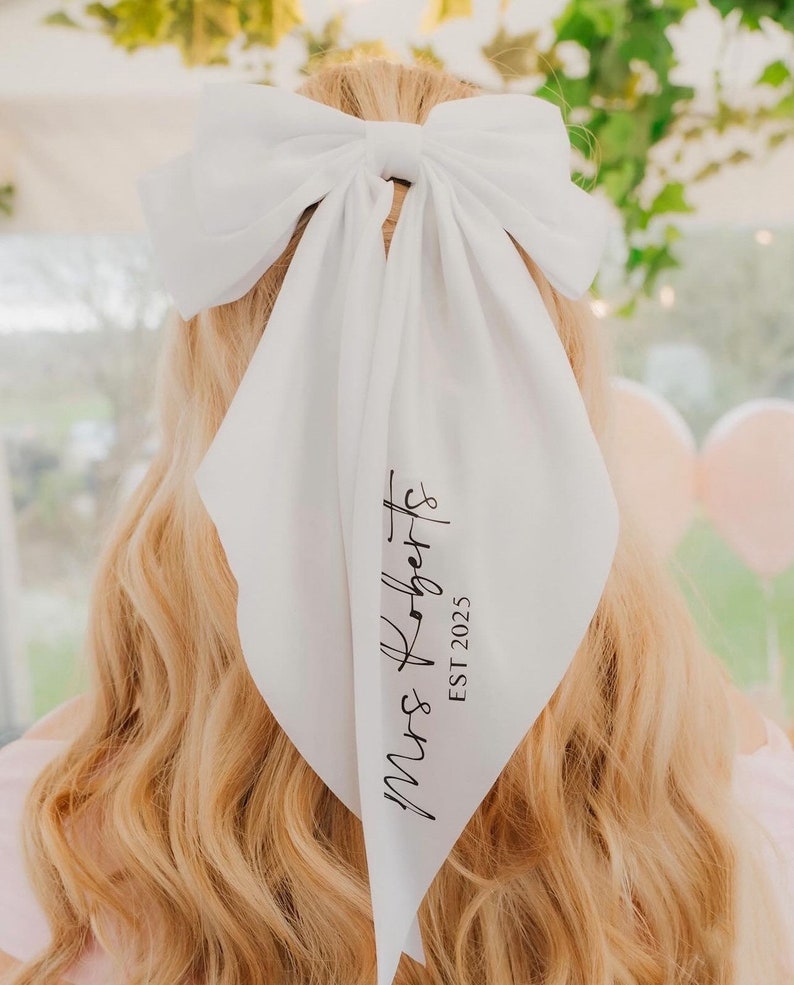 May include: White satin hair scarf with a large bow and the text "Mrs. Roberts EST 2025" printed in black.