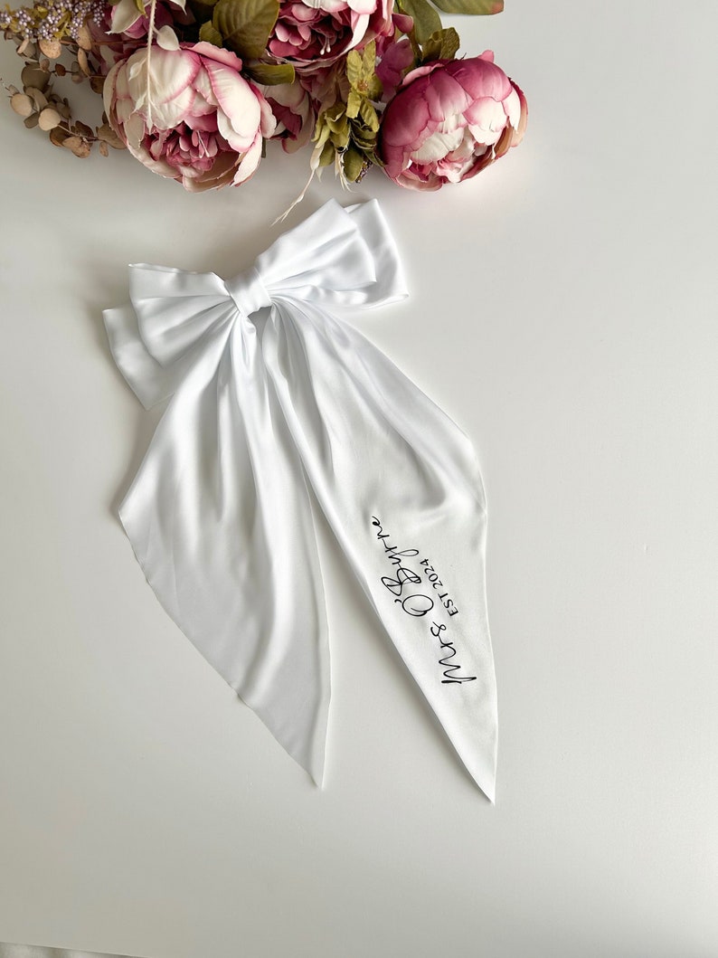 May include: White satin ribbon with a bow and the text "Mrs & Mrs Est 2024" printed on it.