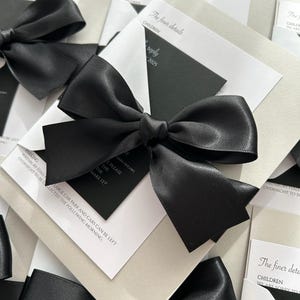 Pode incluir: Cart&otilde;es de convite de casamento preto e branco com la&ccedil;os de fita de cetim preto. O texto nos cart&otilde;es diz "The finer details" e "Children".