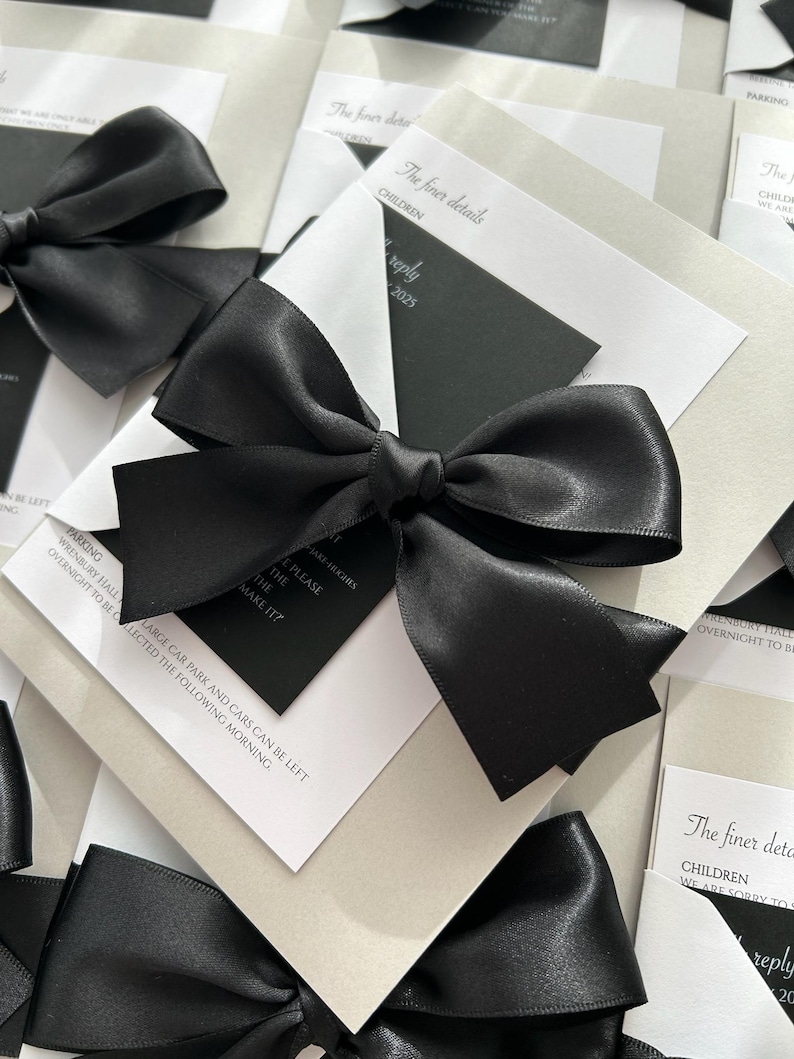 Pode incluir: Cart&otilde;es de convite de casamento preto e branco com la&ccedil;os de fita de cetim preto. O texto nos cart&otilde;es diz "The finer details" e "Children".