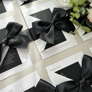 Pode incluir: Cart&otilde;es de convite de casamento preto e branco com la&ccedil;os de cetim preto. O texto nos cart&otilde;es diz "Os detalhes mais finos" e inclui informa&ccedil;&otilde;es sobre estacionamento, crian&ccedil;as e detalhes de resposta.
