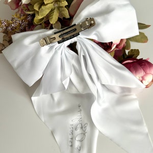 May include: White satin bow with a silver clip and the text "My-B 2021 EST" written on the tail.