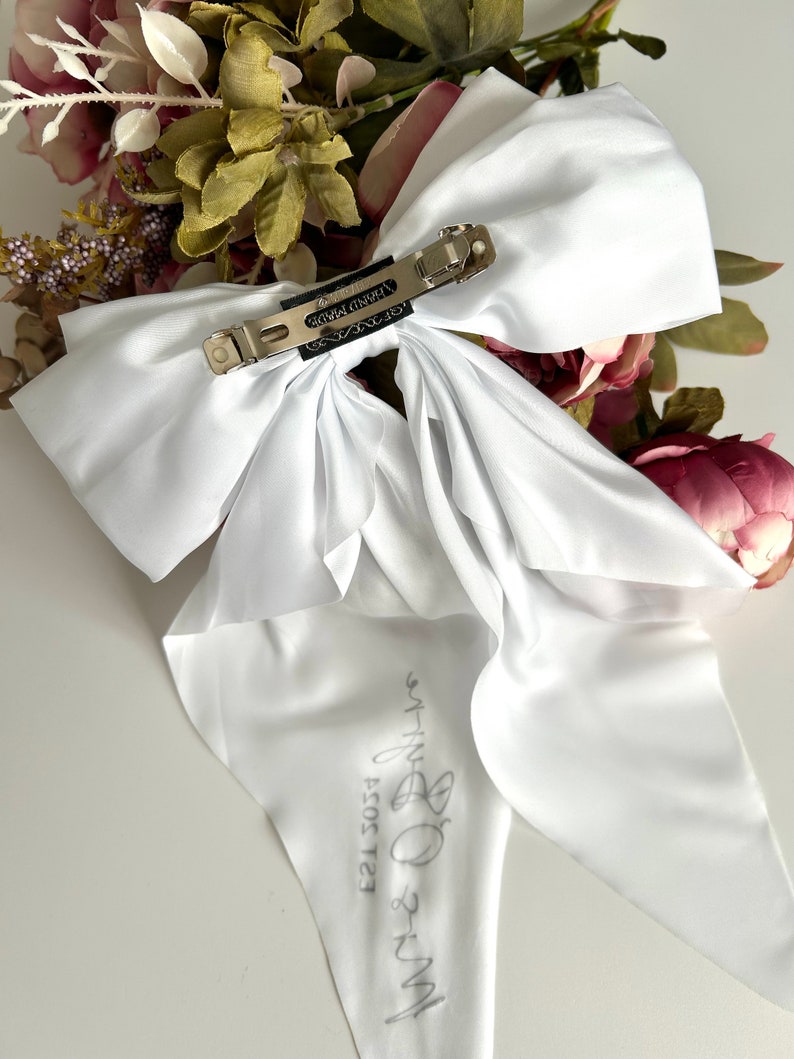 May include: White satin bow with a silver clip and the text "My-B 2021 EST" written on the tail.