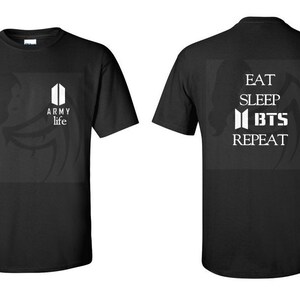 May include: Black t-shirt with a white graphic on the front that says "ARMY life" and a white logo. The back of the shirt has a white graphic that says "EAT SLEEP BTS REPEAT".