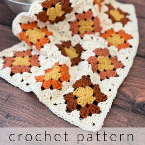May include: Crochet pattern featuring a square with a flower design in shades of orange, brown, and yellow. The square is made with white yarn.