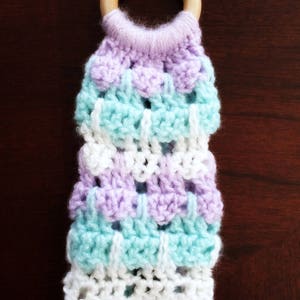 May include: A crocheted baby teether with a wooden ring. The teether is made with a multi-colored yarn in shades of purple, blue, and white.