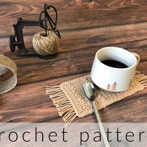 Puede incluir: Un posavasos de ganchillo con flecos, una taza blanca con un diseño de árbol y una cuchara de plata sobre una superficie de madera. El posavasos es beige y la taza tiene un asa marrón.  "crochet pattern" está escrito en blanco en la parte inferior de la imagen.