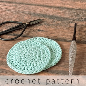 May include: Two crocheted coasters in a light green color, with a crochet hook and scissors in the background. The text "crochet pattern" is visible at the bottom of the image.