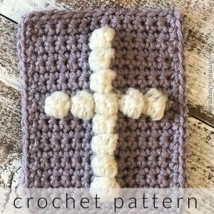May include: A crocheted square in a muted purple color with a white cross design. The cross is made with a textured, raised stitch, and the text "crochet pattern" is at the bottom.