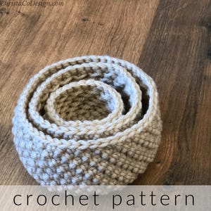 May include: Three crocheted baskets in beige, nested together. The baskets are made with a simple stitch and have a natural, rustic look. Crochet pattern.