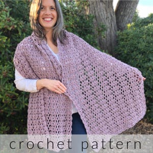 May include: A crocheted shawl in a light purple color with a lacy pattern. The shawl is draped over a person's shoulders and is being held in place by one hand. The text "crochet pattern" is visible at the bottom of the image.